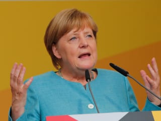 Angela Merkel mit erhobenen Händen an einem Rednerpult 