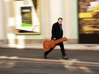 Philipp Fankhauser mit Gitarrenkoffen auf dem Weg zu einem unbekannten Ziel auf einem Bild, das viel Bewegung zeigt.