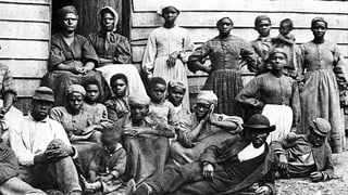 Schwarze Sklaven posieren vor einer ärmlichen Hütte.