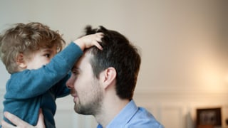 Ein kleiner Junge verwuschelt die Haare eines Mannes. 