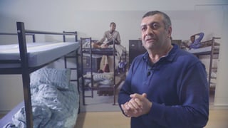 Mano Khalil steht in einem Flüchtlingszimmer mit Hochbetten.