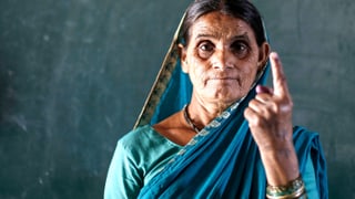 Frau in Indien hält den Finger hoch, der gefärbt ist.