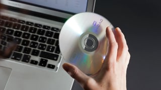 Hand mit DVD vor Computer