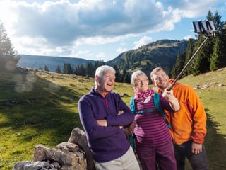 Seniorenpaar mit jüngerem Mann macht ein Selfie auf einer Wanderung in den Bergen.