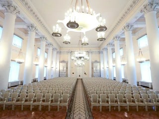 Der weisse Ballsaal vom Smolny-Institut: Weisse Stühle sind symmetrisch angeordnet, in der Mitte liegt ein langer Teppich, der bis zur Türe reicht.