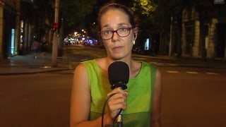 Frau spricht in ein Mikrofon, sie steht des Nachts auf einer Strasse.