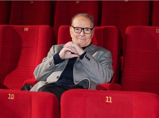 Ennio Morricone sitzt in einem Kino mit roten Sesseln. 