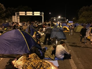 Flüchtlinge sitzen auf der Strasse. Es ist Nacht. Viele Zelten sind aufgespannt.