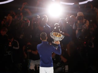 Novak Djokovic von hinten, vorne alles Fotografen und ein Scheinwerfer, der auf den Serben zielt.
