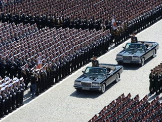 Zwei Autos fahren an stehenden Soldaten vorbei.
