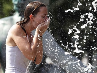 Eine junge Frau spritzt sich Wasser ins Gesicht.