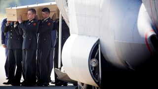 Soldaten tragen einen Sarg auf ihren Schultern aus einem Transportflugzeug.