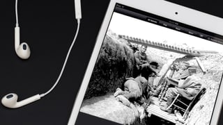Auf einem Smartphone ist ein Bild aus dem Ersten Weltkrieg zu sehen, daneben liegen Kopfhörer.