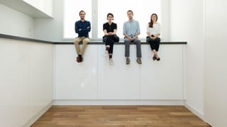 Vier Menschen sitzen in einer überdimensional grossen Küchen auf einer ABlagefläche. 