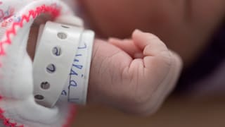 Arm mit Namensschild am Handgelenk eines Neugeborenen