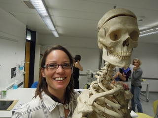 Eine lachende Frau neben einem Skelett.