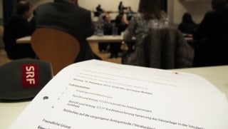 Traktandenliste der Sitzung, im Hintergrund unscharf die Parlamentarier an der Sitzung.