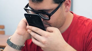 Ein Mann mit Sehbehinderung hält sein Smartphone nahe ans Gesicht.