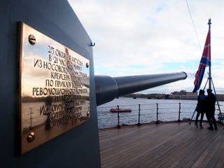 Das Kriegsschiff Aurora mit einer goldenen Aufschrift. Auf dem heutigen Museumsschiff stehen zwei Touristen.