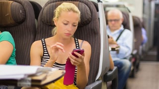 Eine Frau sitzt im Zug und tippt auf ihrem Handy.