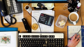 Pult mit Tastatur, Kaffee, Telefon und Taschenrechner.