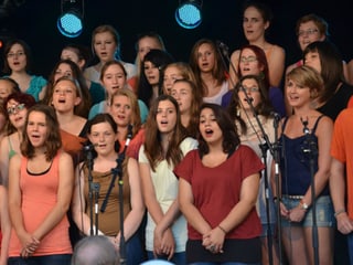 Die jungen Sängerinnen bilden einen Chor und singen in die Mikrofone.