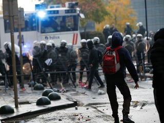 Szene einer Strassenschlacht in Brüssel. Im Vordergrund ein Demonstrant. Im Hintergrund Polizisten in Montur.
