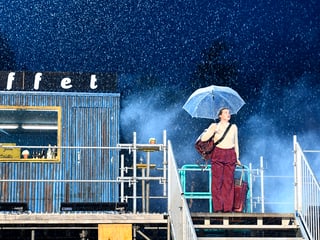 Eine Schauspielerin steht bei ströhmendem Regen auf der Bühne.