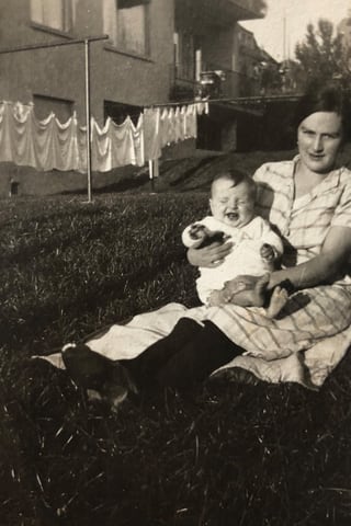 Die Mutter sitzt auf einer Wiese und hält Baby-Betli im Arm.