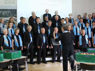 Ein Chor mit Sängerinnen und Sängern, die einen hellblauen Schal oder eine hellblaue Krawatte tragen.