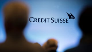 Zwei Menshcen stehen vor dem Logo der Bank Credit Suisse.