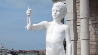 Eine weisse Skulptur zeigt einen Jungen, der eine Kröte in der Hand hält. 