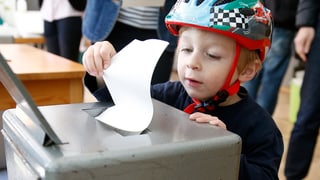 Ein Junge steckt den Abstimmungszettel seines Vaters in die Urne.