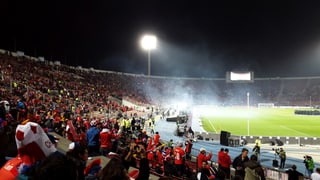 Blick in ein Fussballstadion bei Nacht mit rot gekleideten Fans.