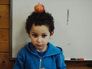 Schauspielbub mit Apfel auf dem Kopf vor einer weissen Wandtafel