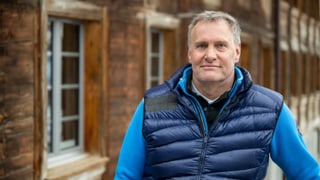 Ein Mann blickt freundlich in die Kamera. im Hintergrund ist ein Holzhaus zu erkennen. Ein Mann blickt freundlich in die Kamera. im Hintergrund ist ein Holzhaus zu erkennen.