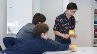 Zwei Jungen strecken sich, um mit Hämmern aus Plüsch ein Kärtchen auf einem Tisch zu erreichen. Eine stehende Frau holt ebenfalls mit einem solchen Hammer aus. Zwei Jungen strecken sich, um mit Hämmern aus Plüsch ein Kärtchen auf einem Tisch zu erreichen. Eine stehende Frau holt ebenfalls mit einem solchen Hammer aus.