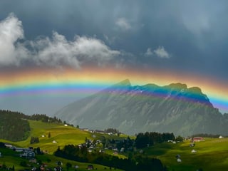 Grosser Regenbogen mit klaren Farben vor Bergwelt. 