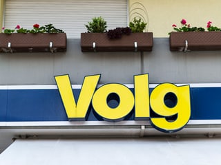 Volg-Logo unter einem Balkon mit Pflanzenkübeln.
