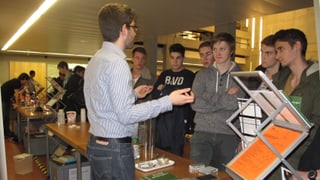 Ein Student informiert an einem Infostand eine Gruppe Schüler über sein Studium.