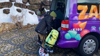 Gaël und Angela stehen vor dem violetten «Zambo-Bus» und legen das Snowboard in den Kofferraum.