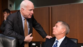 John McCain (links) spricht stehend mit dem neben ihm sitzenden Lindsey Graham.