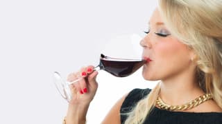 Eine attraktive, blonde Frau trinkt genüsslich ein Glas Rotwein.