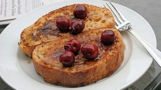 Zwei Scheiben Brot, mit Kirschen verziert, auf einem Teller. 