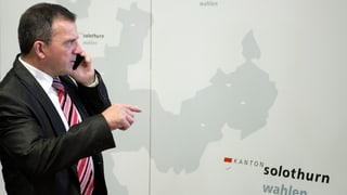 Walter Wobmann am Telefon vor einem Plakat des Kantons Solothurn