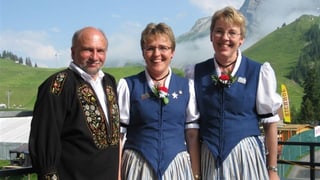 Jodelduett und Akkordeonist tragen Trachten und stehen vor Bergkulisse.