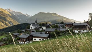 Ein Dorf im Morgenlicht, dahinter verschneite Berge.