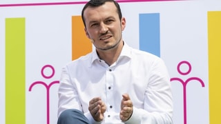 Ein Mann mit Mikrofon sitzt vor einer farbigen Plakatwand. Ein Mann mit Mikrofon sitzt vor einer farbigen Plakatwand.