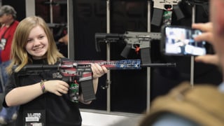Ein Mädchen posiert mit einer Waffe. 