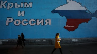 Ein Plakat mit den Umrissen der Krim in russischen Farben, Menschen gehen vorbei.